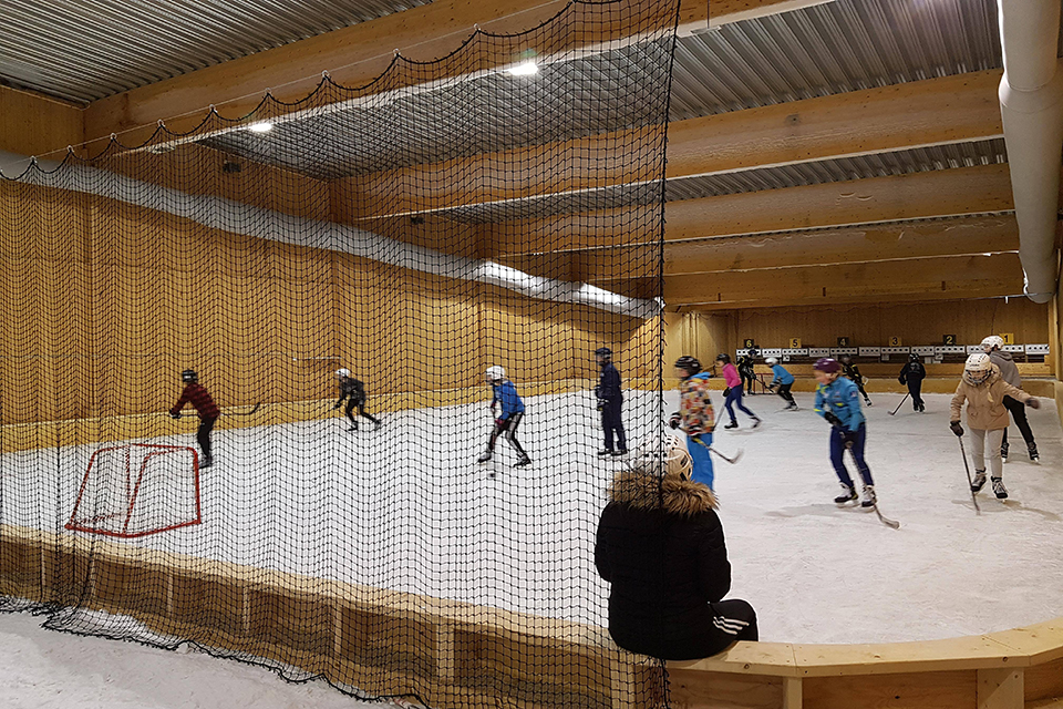Bilden visar vår skridskobana fylld med åkande barn som spelar hockey. 