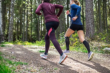 Två kvinnliga motionärer joggar på motionsbanorna i grönskande skogen. 
