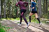 Två kvinnliga motionärer joggar på motionsbanorna i grönskande skogen. 